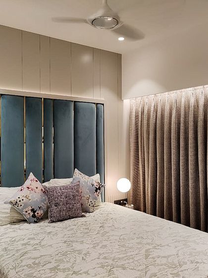 A bedroom in the Jesrani Residence featuring a plush, floor-to-ceiling velvet headboard with brass inlay. The combination of soft texture and metallic detail adds a touch of understated glamour to this minimalist room.