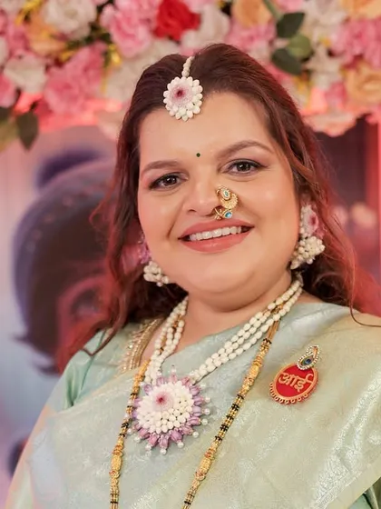 A happy client portrait showing the floral maang tikka, necklace, and 'Aai' brooch from her custom baby shower set.