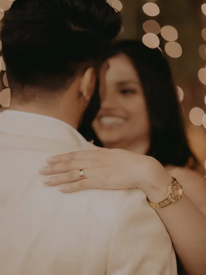 A creative focus on the engagement ring as the bride embraces her fiancé, her happy smile blurred softly in the background.