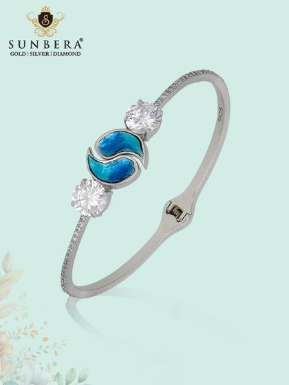 A modern silver kada bracelet with a central blue enamel motif and two large side stones. This piece is a perfect blend of colour, sparkle, and contemporary design.