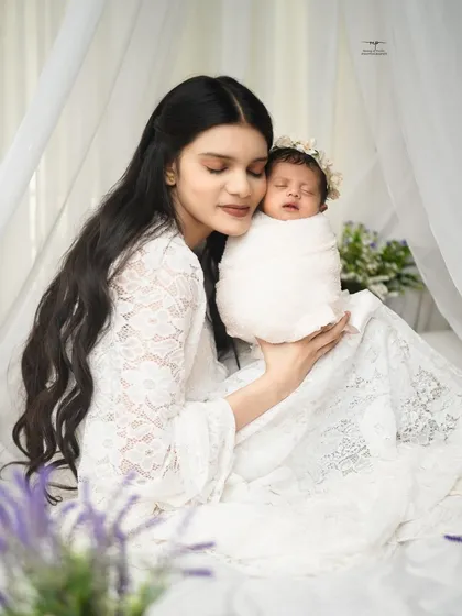 A mother's gentle love, captured in a serene portrait with her newborn. Dressed in white lace, she holds her sleeping baby, creating a timeless and angelic image.