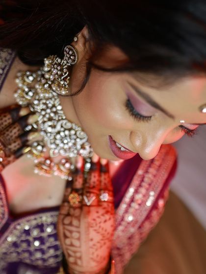 A close-up shot capturing the bride's beautiful makeup and jewellery, with her henna-adorned hands framing her face.