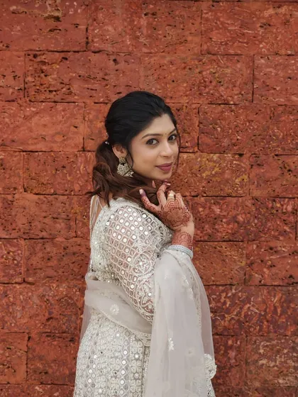 A chic and modern look for a wedding guest. She is wearing a white Anarkali, and her makeup is subtle yet defined, paired with a stylish ponytail.