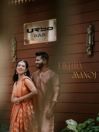 A happy, sun-kissed photo from a Haldi or Mehendi event. The couple's coordinated outfits and the rustic wooden background create a warm and joyful vibe.