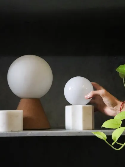 A hand interacts with one of our custom marble and glass lamps. The design invites touch, combining the cool, solid feel of the stone with the smooth, warm glow of the light.