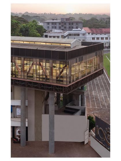 An exterior view of "Hoverspace" at dusk, showing the transparent office interiors and the cantilevered structure. The building becomes a lantern-like beacon for the campus at night.