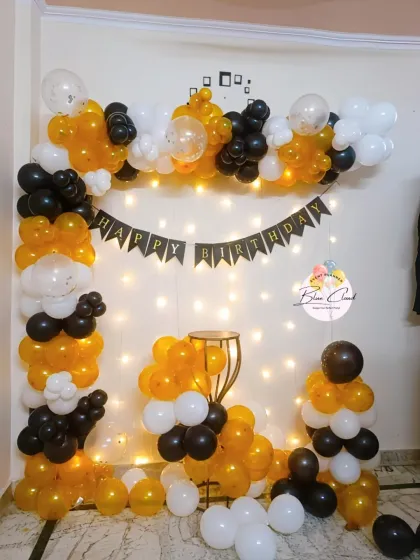 A black, white, and mustard yellow balloon frame with fairy lights for a birthday party.