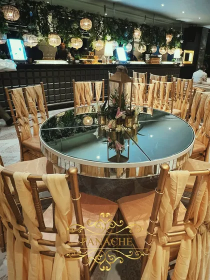 The guest seating area, featuring mirror-top tables that reflect the hanging greenery and lights from the ceiling. Gold chiavari chairs with elegant drapes complete the luxe look.
