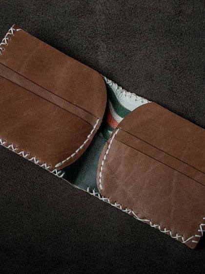 The interior of a hand-stitched leather wallet, showing its card slots and unique design. This piece combines printed fabric with classic brown leather for a personalized touch.