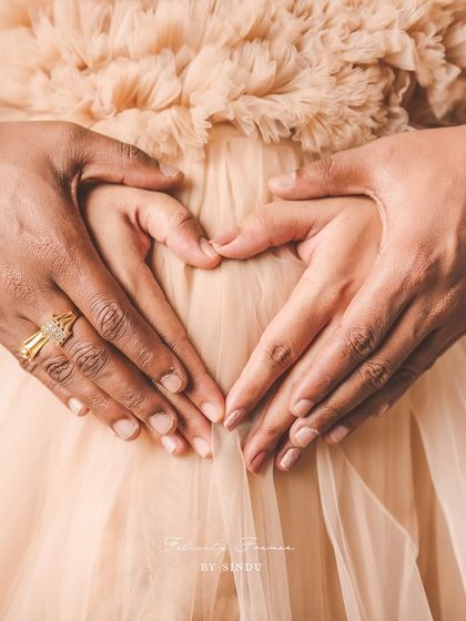 A close-up shot of a couple's hands forming a heart shape on the mother's baby bump. This intimate photo beautifully symbolizes the love and anticipation for their growing family.