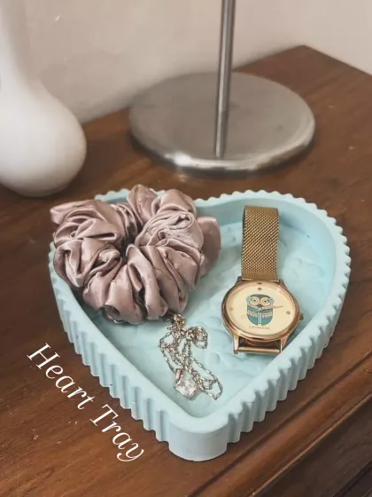 A close-up of our ribbed heart tray in a lovely light blue marble, holding a watch, necklace, and scrunchie. It's the little details that make a space feel like home.