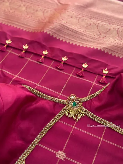 A unique blouse design featuring a jewellery-inspired back piece with an emerald green stone, set on a checked pink silk fabric.