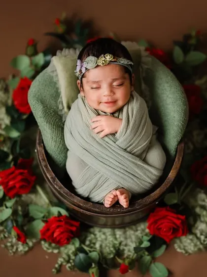 A sleeping beauty surrounded by roses. This newborn is swaddled snugly in a sage green wrap, creating a beautiful color contrast with the red flowers. This is an example of a creative, posed newborn portrait.