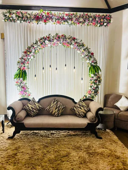 We can transform any corner of your home into an elegant space for an engagement or small party. This setup features a circular floral arch with mixed fresh flowers and hanging Edison bulbs, creating a modern and sophisticated backdrop for your special moments.