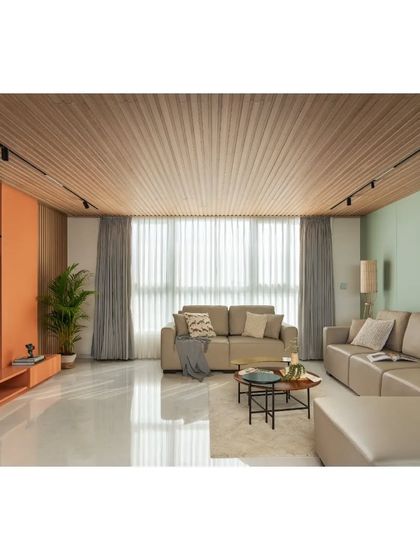 The living room in the House Above The Tree features a slatted wood ceiling and a soft, neutral color palette. The full-height windows and sheer curtains allow for ample natural light while maintaining privacy.