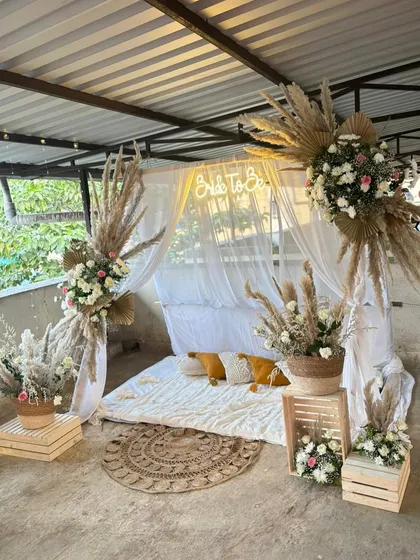 A dreamy, Pinterest-worthy bridal shower with a boho theme. The setup includes a canopy of white drapes, pampas grass arrangements, and a cozy floor seating arrangement.