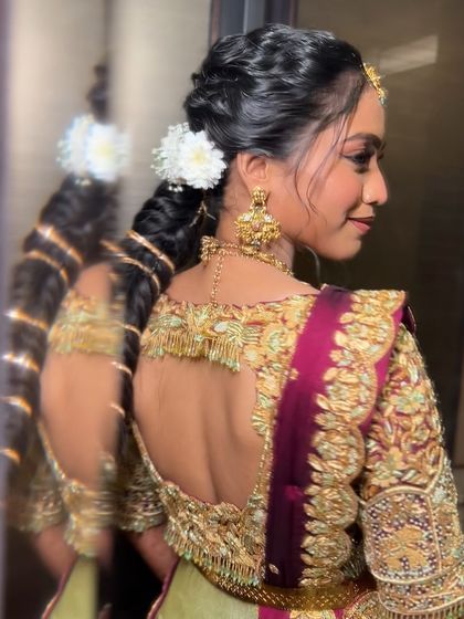 A side profile of a bride with a modern textured braid, adorned with a simple white flower and gold jewellery.