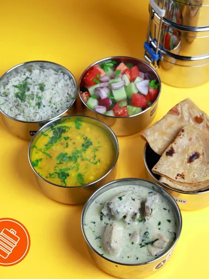 A look inside our non-veg tiffin, packed in our signature steel dabbas. This meal features a creamy chicken curry, dal, rice, salad, and rotis.