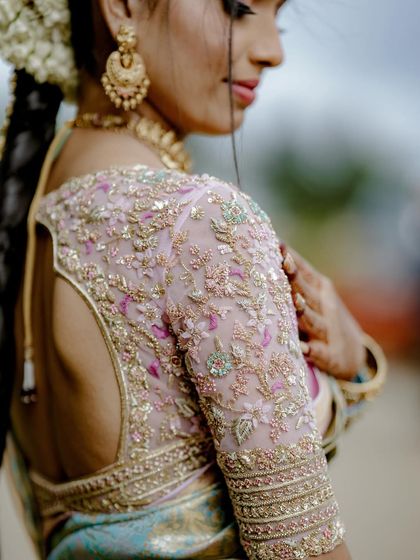 A close-up on the sleeve of the bride's blouse, showing the detailed floral embroidery in shades of pink and green on a sheer fabric.