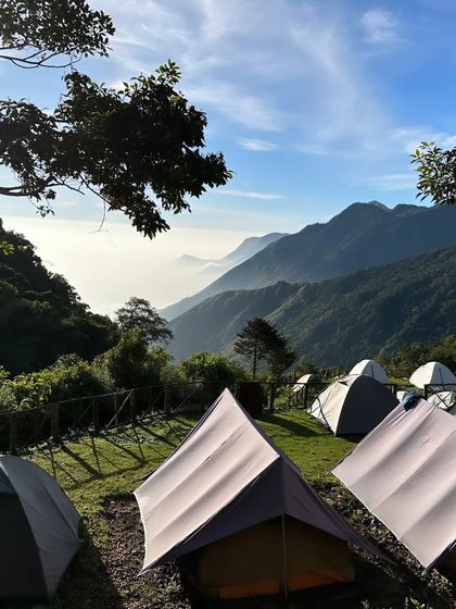 Tents pitched on the green hillside of the Munnar camp, with layers of mountains visible in the distance.