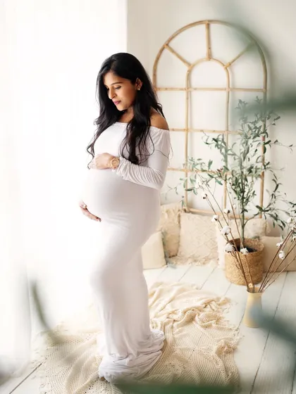 Simplicity is so beautiful. This gorgeous mommy is dressed in a classic, form-fitting white gown, standing by a window that fills the room with soft, natural light.