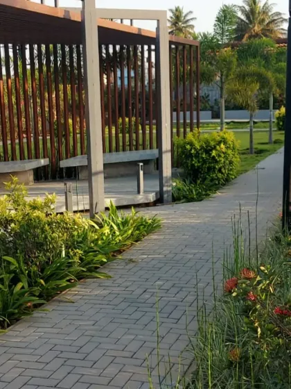 A park pathway leading to a modern seating area with a slatted wood screen. The landscaping includes a mix of shrubs and flowers for color and texture.
