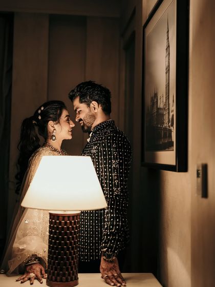 An intimate portrait using creative lighting. The warm glow of the table lamp illuminates the couple's faces, creating a moody, romantic, and cinematic feel for their reception look.