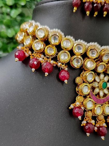 A close-up of the necklace, showing the large kundan stones and red bead details.