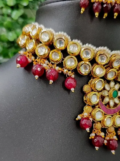 A close-up of the necklace, showing the large kundan stones and red bead details.
