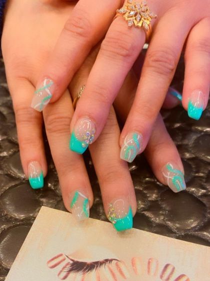 A fresh and modern take on the French manicure. This set features clear extensions with a bright turquoise tip, white line art, and delicate crystal accents.