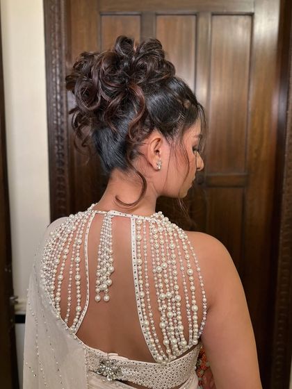 A back view of the tousled high bun, showcasing the intricate, messy-chic styling and how it complements the pearl-draped blouse.