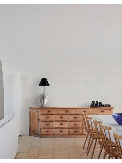 A table lamp from the 'Bernard and friends' collection sits atop a rustic wooden credenza. The lamp's simple, elegant form and natural wood texture bring a sense of calm and craftsmanship to the dining space.