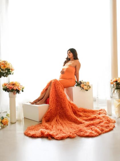 A beautiful portrait of a mother-to-be seated like a queen, her vibrant orange gown cascading around her.
