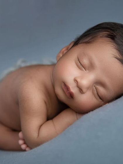 A close up of the side pose on a blue backdrop, focusing on the baby's peaceful, sleeping face.