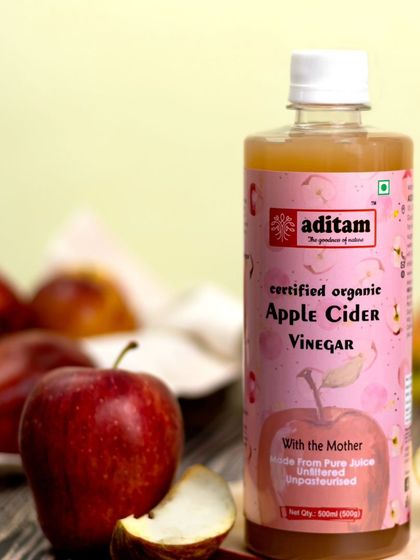 A close-up of the apple cider vinegar bottle, with fresh red apples in the foreground. This composition emphasizes the product's primary ingredient and creates a fresh, appealing visual.