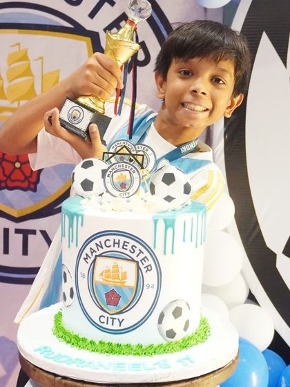 The birthday boy holds his trophy proudly with his incredible Manchester City themed cake, a true winner's celebration.