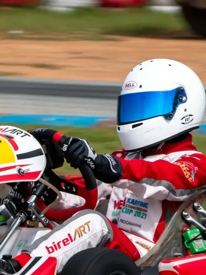 A driver in a Birel ART kart with number 42, focused and ready, navigating a turn during a race.