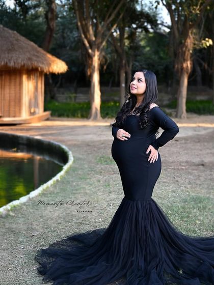 A serene outdoor portrait. The mom-to-be in a classic black gown stands by the water, creating a peaceful and beautiful image in natural surroundings.