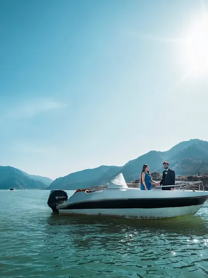 A wide-angle shot showing the grandeur of Tehri Lake. The small boat against the vast landscape emphasizes the feeling of a private, intimate escape for the couple.