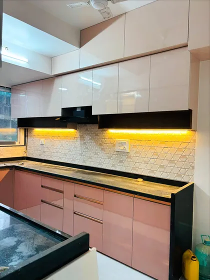 A vibrant U-shaped kitchen showcasing a stylish pairing of blush pink and glossy white cabinets. The design is complemented by a geometric tile backsplash, a sleek black granite countertop, and functional under-cabinet lighting.