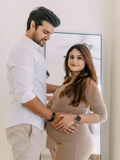 The partner stands behind, gently holding her belly as she looks confidently at the camera. This pose is a beautiful blend of a classic portrait and an intimate couples moment.
