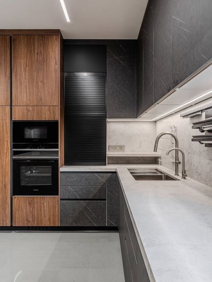 Warm contrast takes center stage in this Ahmedabad kitchen. Deep walnut wood meets the quiet drama of matte black fronts, while a seamless quartz counter and backsplash create a monolithic sweep.