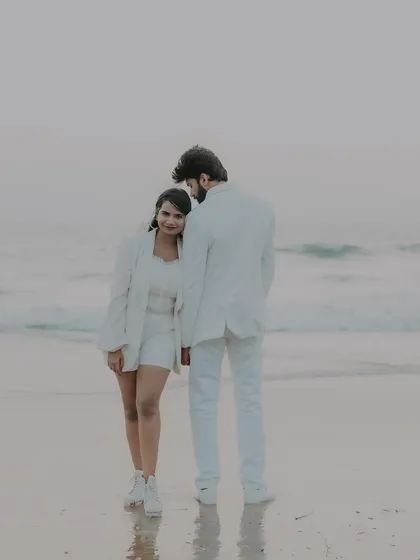 A serene moment on the beach as the sun sets. The couple stands by the water, creating a peaceful and romantic silhouette against the evening sky.