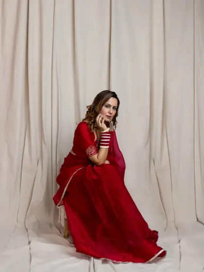 A simple, elegant portrait that highlights the subject's poise. The neutral background ensures all focus remains on her, the vibrant red of the saree, and her confident expression.