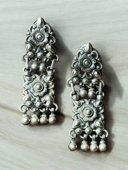 A pair of long, rectangular oxidised silver earrings. The design features intricate floral work and small dangling ghungroos.