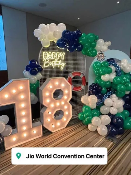 An 18th birthday with a nautical theme at the Jio World Convention Center. The setup includes marquee numbers, a "Happy Birthday" neon sign, and a balloon arrangement in navy, green, and white.