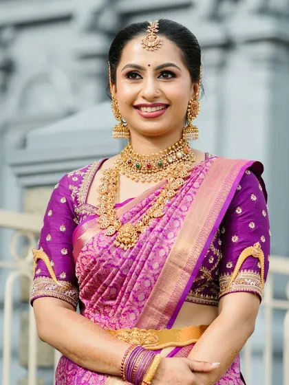 A close-up of a bride in her vibrant purple Kanchipuram saree. The custom blouse features unique embroidered motifs on the sleeves, adding a personal touch to her traditional attire.