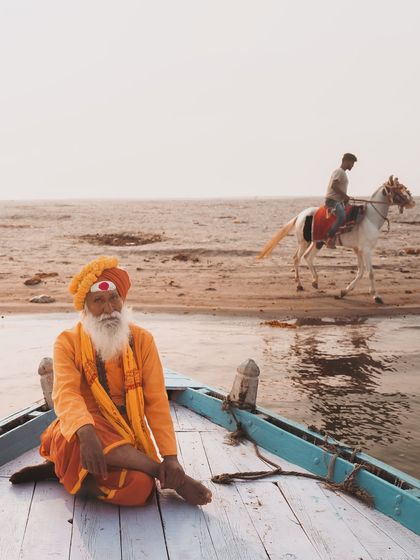 A sadhu sits peacefully at the bow of a boat on the Ganga, while in the background, life continues on the sandy banks. This frame captures the serene and contemplative pace of life in Varanasi.