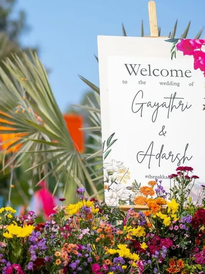 A custom welcome sign for the wedding of Gayathri and Adarsh, nestled in a bed of colorful wildflowers.