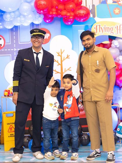 The birthday boys posing with staff members dressed as a pilot and a bus conductor, perfectly fitting the travel theme.